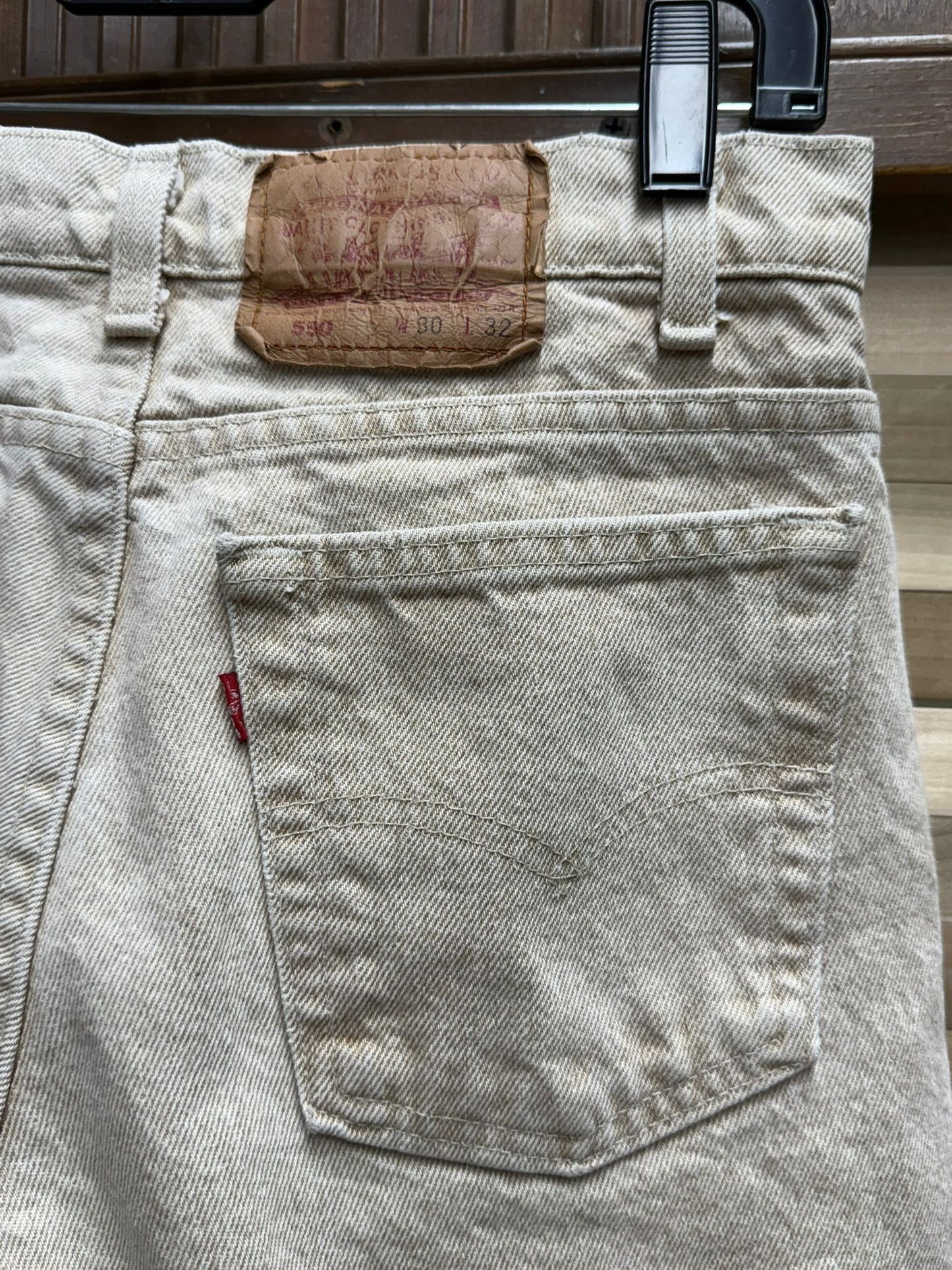 Close-up of light gray jeans with a Levi's tag and button on a wooden surface.