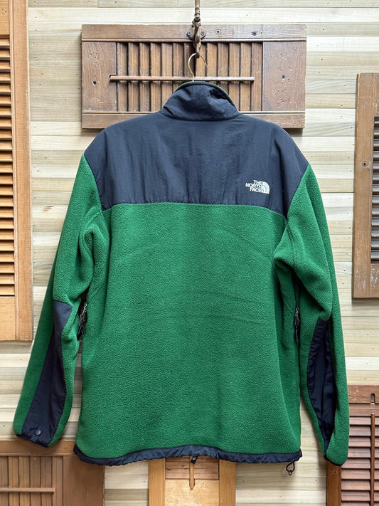 Green and navy fleece jacket with The North Face logo on a wooden background