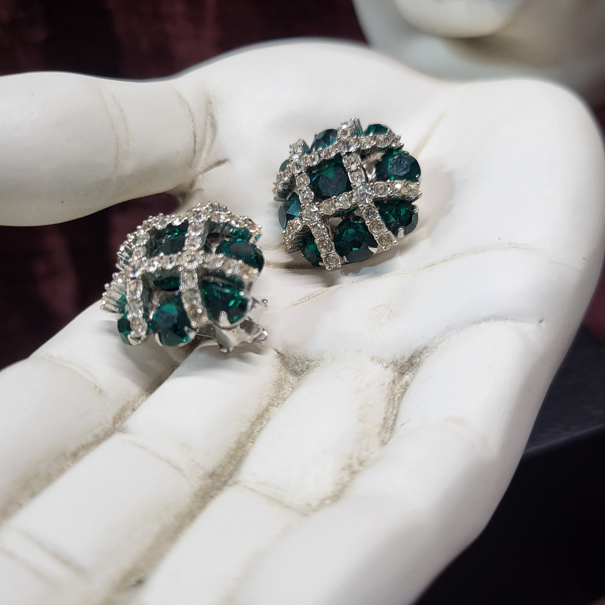 Pair of green gemstone earrings held in white gloves on a marble surface