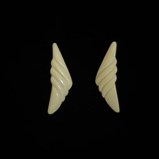 Pair of beige wing-shaped earrings on a black background