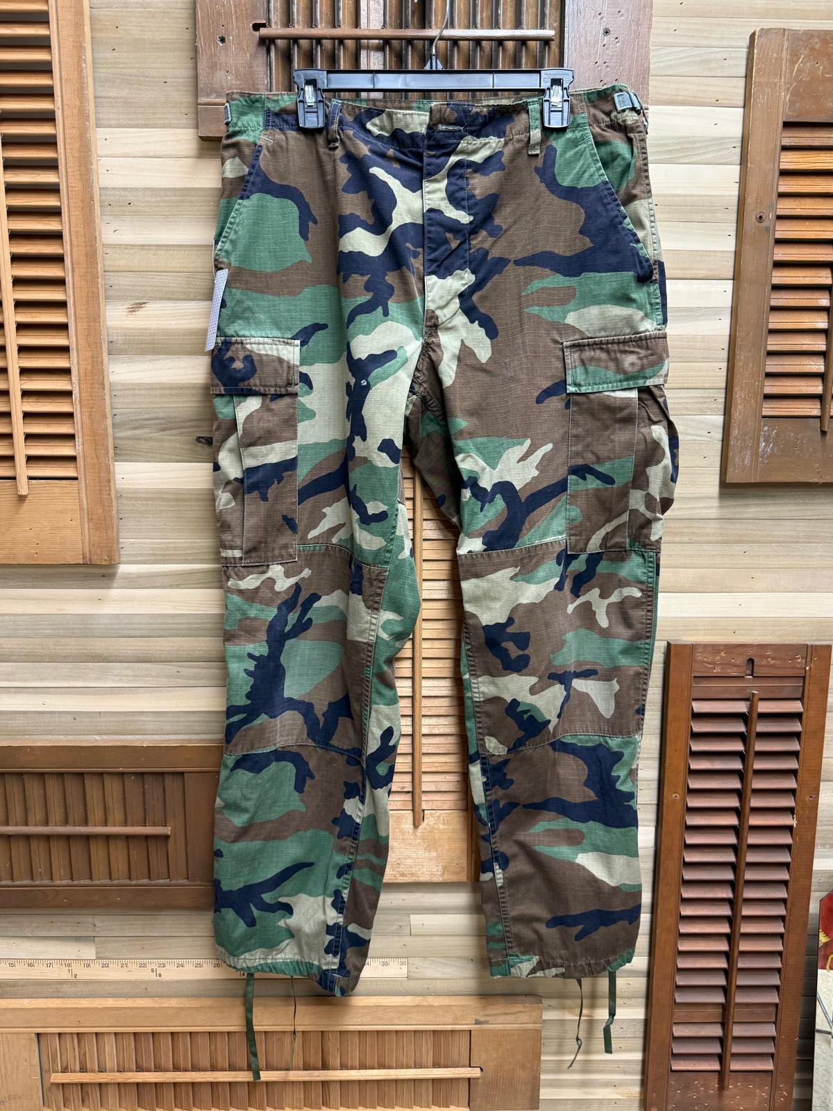Camouflage pants hanging on a wooden rack against a wooden panel background