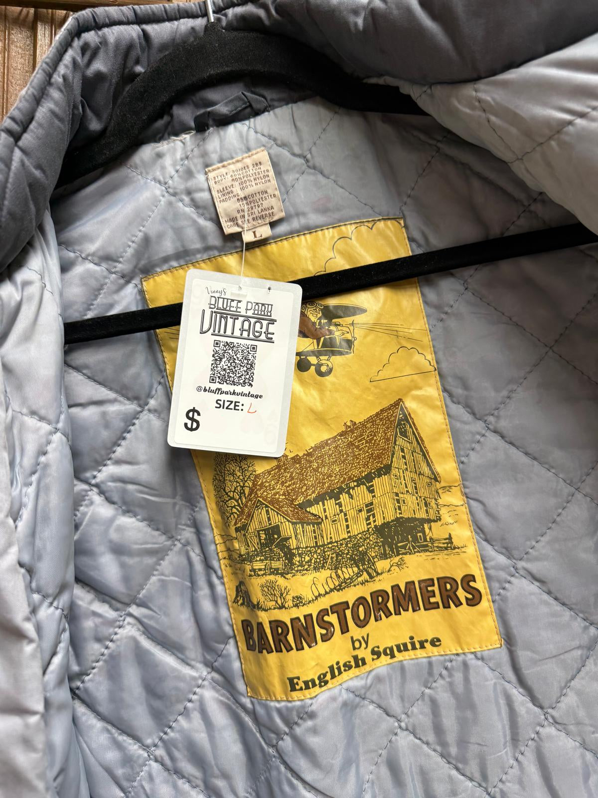 Gray quilted jacket with a Barnstormers by English Squire tag on a wooden surface