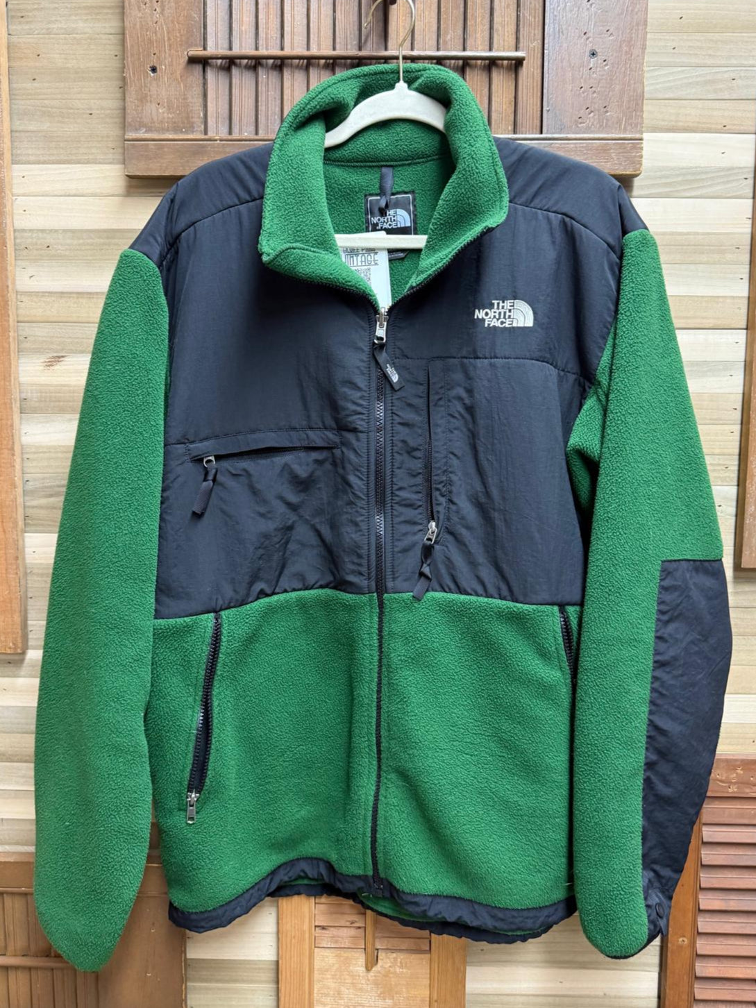 Green and navy fleece jacket with 'The North Face' logo on a wooden background