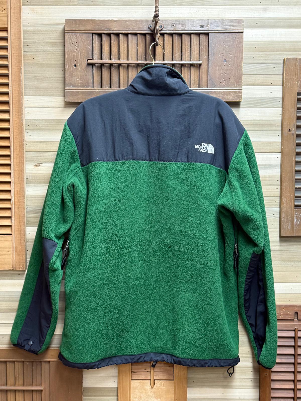 Green and navy fleece jacket with The North Face logo on a wooden background